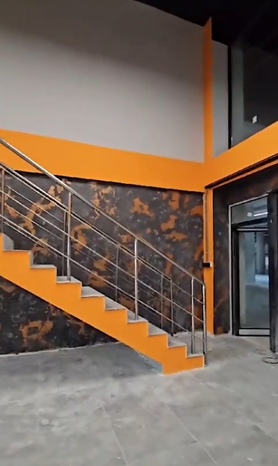 Merdiven boşluğunda turuncu detaylarla pas-korten efektli duvar